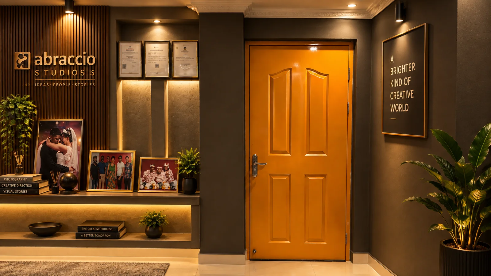 Entrada da sala de fotografia: porta laranja fechada; à esquerda, uma parede com o nome da Abraccio, certificados emoldurados e fotografias de trabalhos; à direita, um quadro com uma frase.