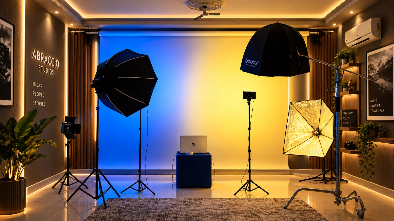 Sala de fotografia 2 com o fundo iluminado a azul e amarelo, dois softboxes, um painel LED e uma girafa, e um portátil sobre um cubo azul ao centro.